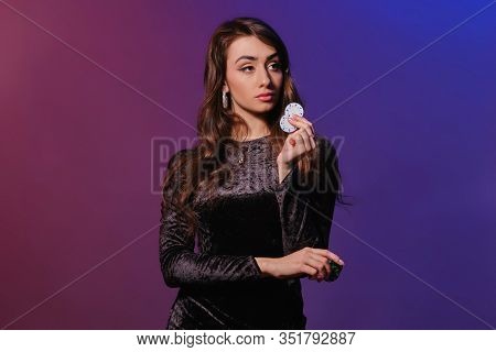 Brunette Woman In Black Velvet Dress Showing Multicolored Chips, Posing Against Coloful Background. 