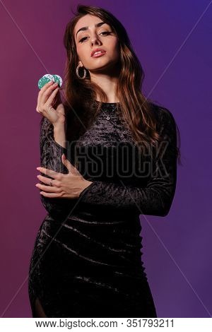 Brunette Woman In Black Velvet Dress Showing Multicolored Chips, Posing Against Coloful Background. 