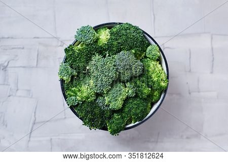 high angle view of some stems of raw broccoli in a bowl, on a white textured surface