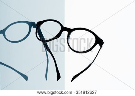 closeup of a pair of black eyeglasses on a reflecting surface against a white background