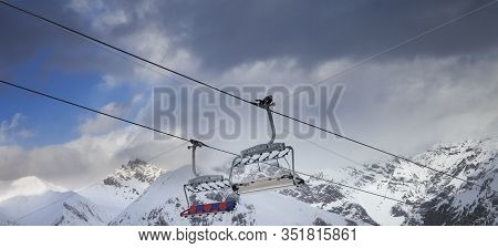 Sunlit Chair Lift, Snowy Ski Slope, High Winter Mountains And Dark Cloudy Sky. Ski Area Mottolino Fu