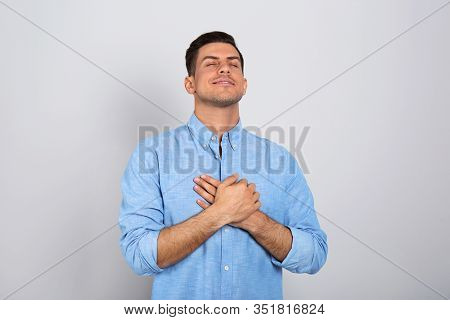 Handsome Grateful Man With Hands On Chest Against Light Grey Background