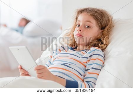 Little Girl In A Hopital Bed Holding The Tablet