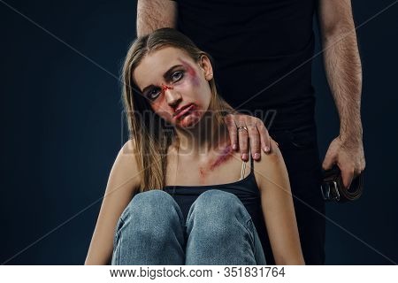 Strong Man Put His Hand On Female Shoulder. Scared Victim With Bruises On Face Sitting Nearby. Blue 