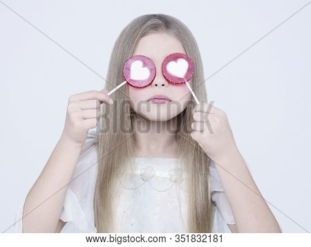 little pretty girl with big candy. Studio ashion photography of kid in white dress. Beautiul model eating sweet lollipop.