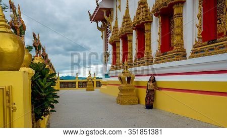 Woman In Sarong Leaning Against Wall Of Wat In Pak Nam Pran Pranburi Thailand.