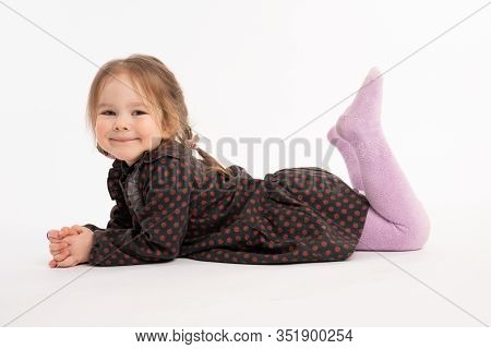 Happy Adorable Redhead Little Girl In Dress Smiling And Looking At The Camera While Liying On The Gr