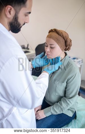 Tall Doctor In Blue Gloves Looking Concentrated While Palping Lymph Nodes Of His Patient