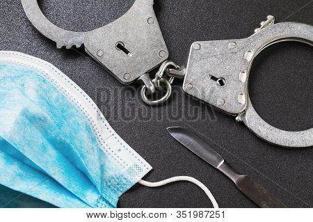 Handcuffs, Scalpel And Medical Mask On The Table. View From Above. Medical Error Concept