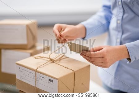 delivery, mail service, people and shipment concept - close up of woman packing parcel box and tying tag by rope at post office