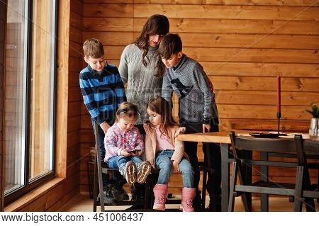 Four Kids With Mother In Modern Wooden House Watching Video In Mobile Phone.
