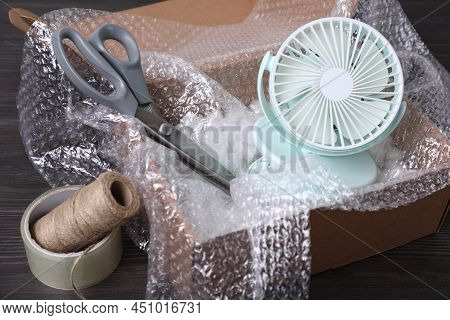 Small Fan With Bubble Wrap In Cardboard Box And Packaging Items On Dark Wooden Table