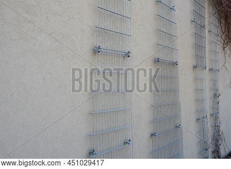 Plaster Concrete Wall On A House Or Factory. On The Wall Are Attached Galvanized Grilles Made Of Che