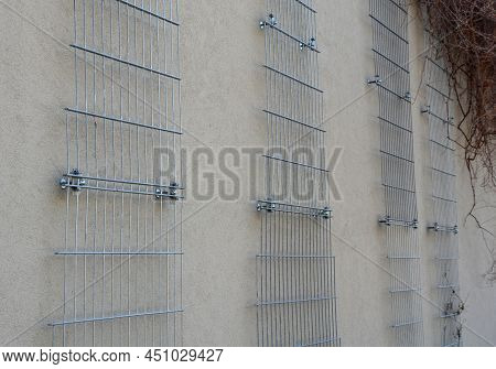 Plaster Concrete Wall On A House Or Factory. On The Wall Are Attached Galvanized Grilles Made Of Che