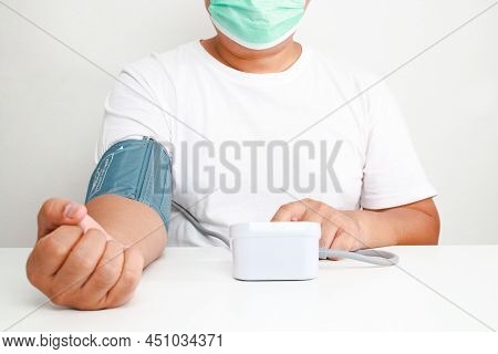 An Obese Man Wearing A Mask Uses A Blood Pressure Monitor On His Arm Himself. Obesity Concept Risk O