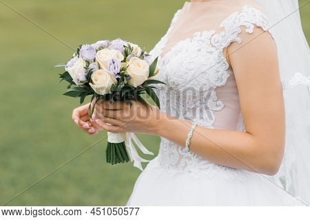 The Bride's Wedding Bouquet Of Milk Roses And Lilac Eustoms In The Hands Of The Bride Close-up