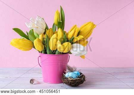 Easter Holiday Decorations: Eggs In Bird Nest And Bouquet Of Yellow Tulips In Bucket On Pink Backgro