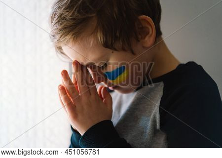 Ukrainian Boy Closed Her Eyes And Praying To Stop The War In Ukraine. Hands Folded In Prayer Concept