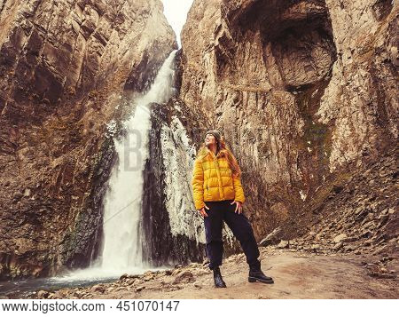 A Woman Looks Up While Standing Against The Background Of An Icy Stormy Waterfall Flowing From A Gor