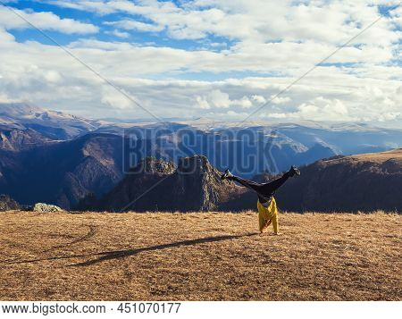 A Girl Makes A Flip On Her Hands In An Autumn Meadow Lit By The Sun, Overlooking A Mountain Valley A