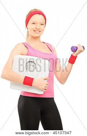 Young female holding a dumbbell and a weigth scale, isolated on white background