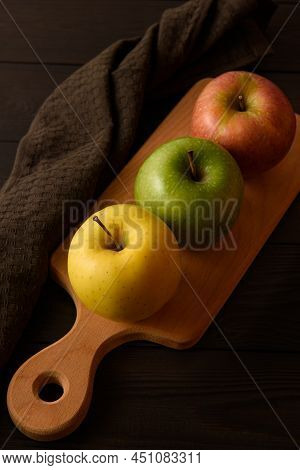 Yellow, Green And Pink Apples Lie On A Wooden Board Next To A Brown Cotton Napkin On A Brown Wooden 