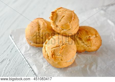 Homemade Profiteroles On A Metal Grid And White Paper On A White Wooden Background.