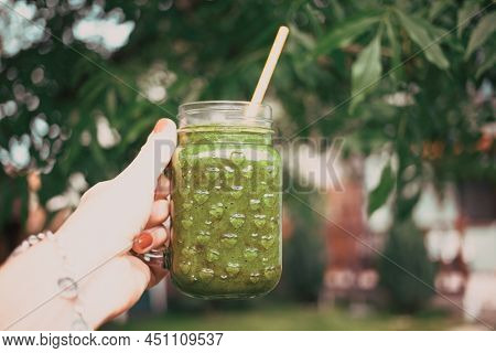 woman's hand holding a jar with green cold-pressed juice, nature background. Healthy eating, detoxing, juicing, body cleancing concept