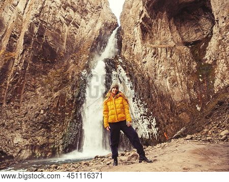 A Smiling Woman Stands Against The Background Of An Icy Stormy Waterfall Flowing From A Gorge Of She