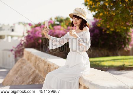 A Woman In Srtaw Hat And White Dress Using Smart Phone Or Taking A Selfie On The Tropical City In Su