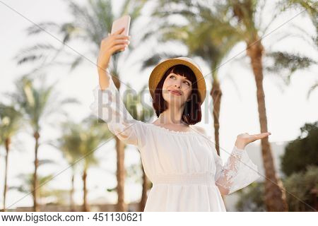A Woman In Srtaw Hat And White Dress Using Smart Phone Or Taking A Selfie On The Background With Pal