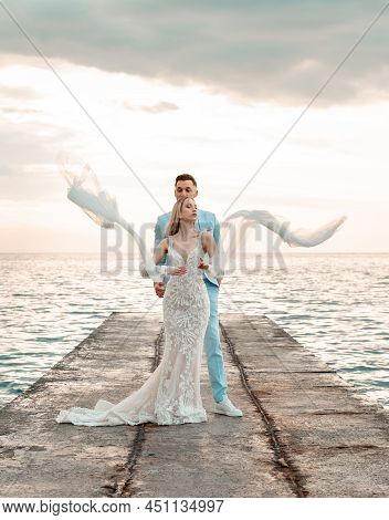 Young Bride, Fashionable, Blonde Model In Luxury Wedding Dress With Groom On The Coast. Girl In Long