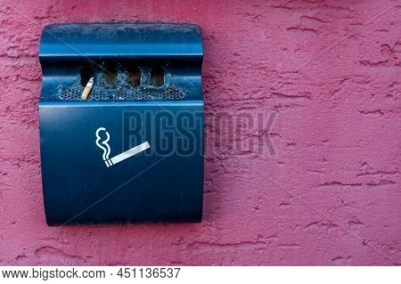 Wall-mounted Trash Can For Ash And Cigarette Butts. Black Garbage Bin On Purple Wall. Smoking Cigare