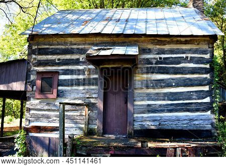 Old, Rustic Log Cabin Has A Rotting Front Porch And A Brown Door.  Historic Cabin Sits Lost In Time 