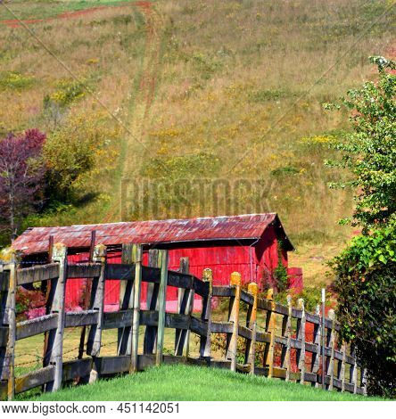 Rustic Wooden Fence Runs In Front Of A Red, Wooden Barn In Tennessee.  Barn Has Rusting Roof, And Si