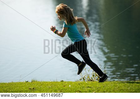 Child Boy Running Or Jogging Near Lake On Grass In Park. Little Runners Jogging Outdoors In Summer N