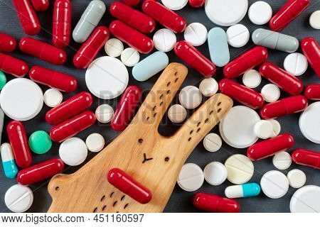 A Wooden Rabbit With A Red Pill Instead Of A Mouth Against A Background Of Many Pills, Pills And Vit