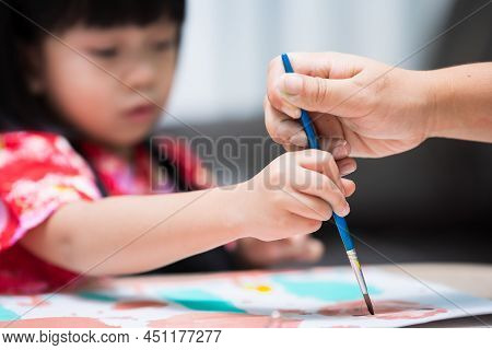 Selective Focus. Mother And Child's Hands Are Holding Brush To Paint Watercolor Onto Paper. Kid Make
