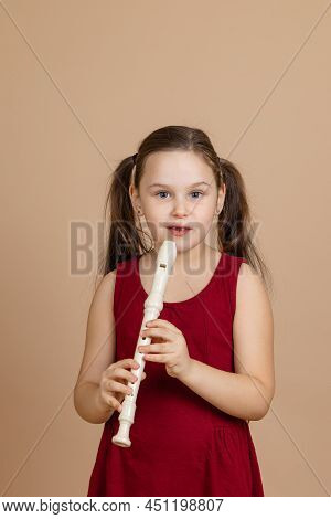 Girl In Red Dress Thoughtfully Hold Common Flute And Pinch Holes On It, Beige Background. Learning T