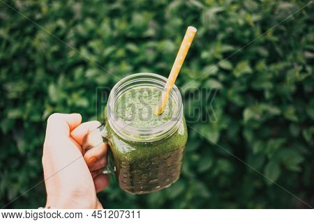woman's hand holding a jar with green cold-pressed juice, nature background. Healthy eating, detoxing, juicing, body cleancing concept