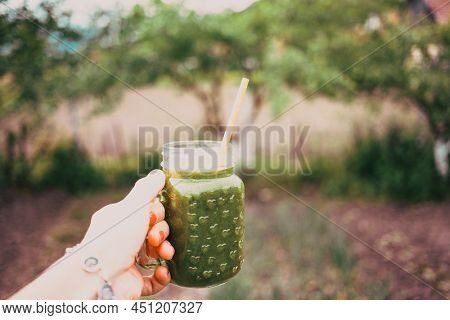 woman's hand holding a jar with green cold-pressed juice, nature background. Healthy eating, detoxing, juicing, body cleancing concept