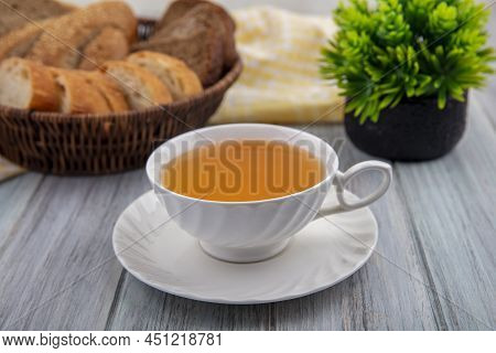 Side View Of Cup Of Hot Toddy On Saucer With Bread Slices In Basket On Plaid Cloth And Plant On Wood
