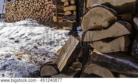 The Firewood Is Stacked In A Woodpile. In The Foreground Is An Axe Stuck In A Split Log. Close-up. S