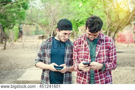 Young Latin Man Spying On Another Cell Phone, Man Showing His Cell Phone To Another Guy, Two Guys Ch