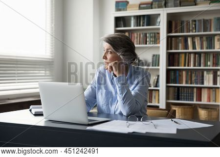 Serious Older Businesswoman Sit At Workplace Desk Staring Out Window