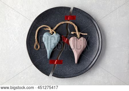 A Broken Plate Is Glued Together With Sticky Tape And Two Decorative Wooden Hearts On A Light Concre