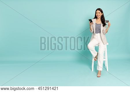 Young Asian Businesswoman Sitting And Showing Credit Card For Making Payment In Mobile Phone Isolate