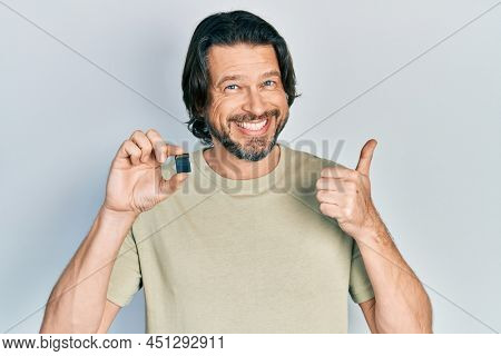 Middle age caucasian man holding sdxc card smiling happy and positive, thumb up doing excellent and approval sign 
