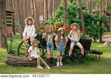 Group Of Friendly Preteen Girls Posing Next To Vintage Wooden Cart Designed As Flower Bed Outdoors