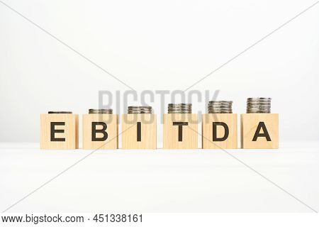 Ebitda Text Written On Wooden Block With Stacked Coins On White Background, Growing Trend, Business 